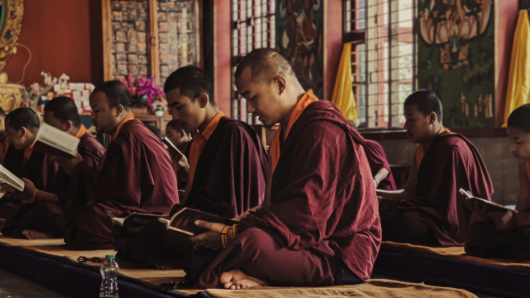 Monks seated indoors reading religious texts during study time inside a Buddhist monastery