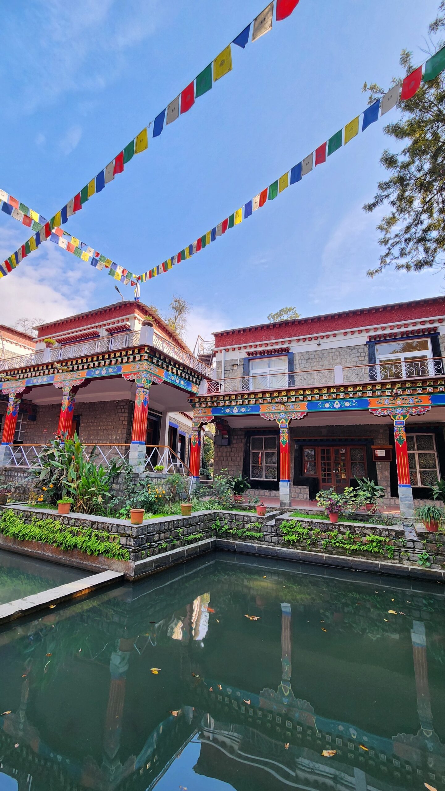 Calm pond inside Norbulingka Monastery in Dharamshala with prayer flags and traditional Tibetan architecture