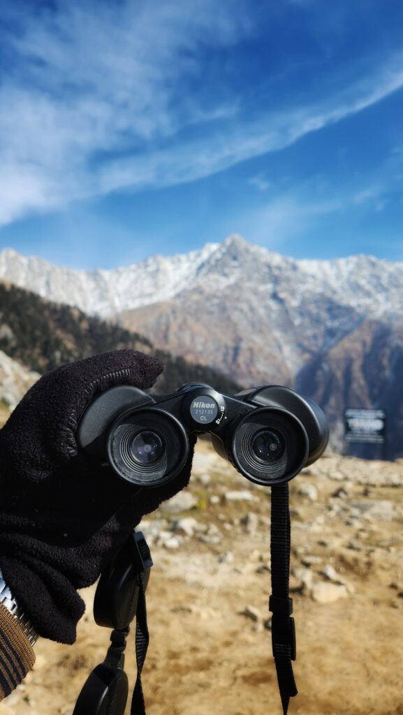 Binoculars held up toward snow-covered Dhauladhar mountains while trekking in Dharamshala