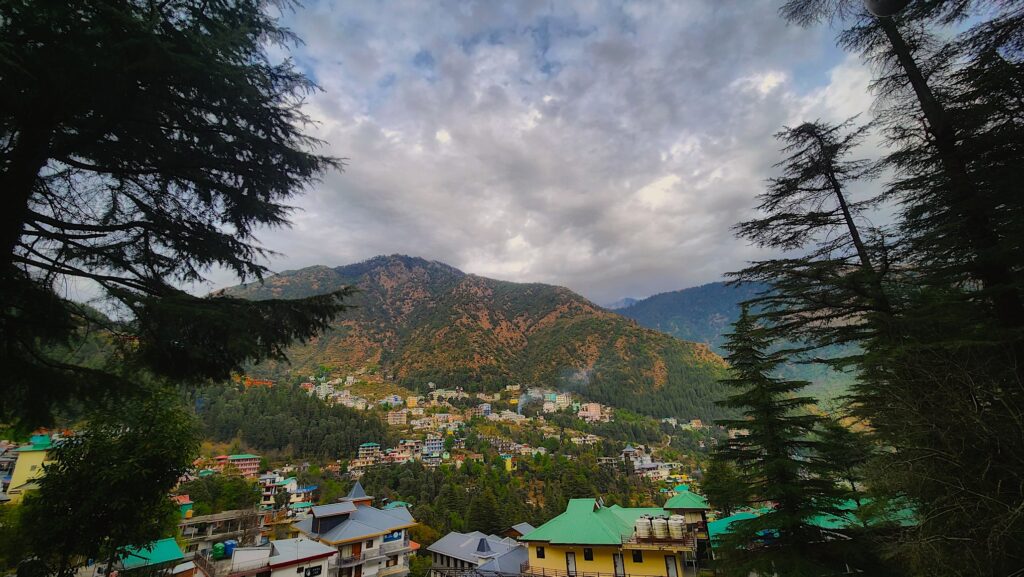 Cloudy hillside view of Dharamshala town surrounded by forests, showing typical mountain weather conditions