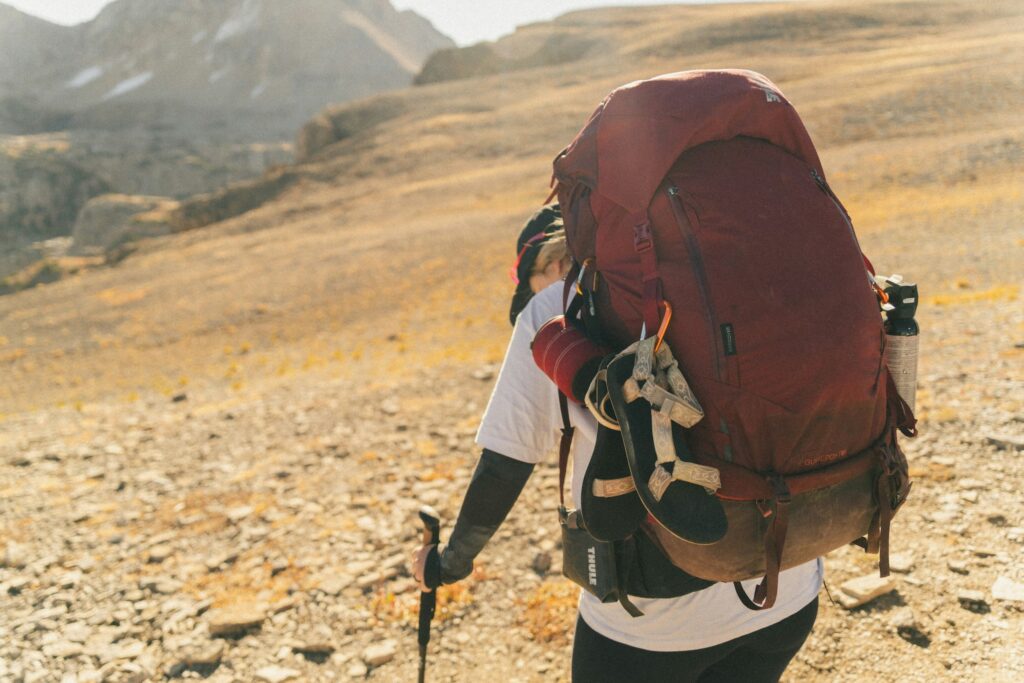 Trekker carrying a large backpack with hiking gear on a rocky high-altitude trail in the Himalayas