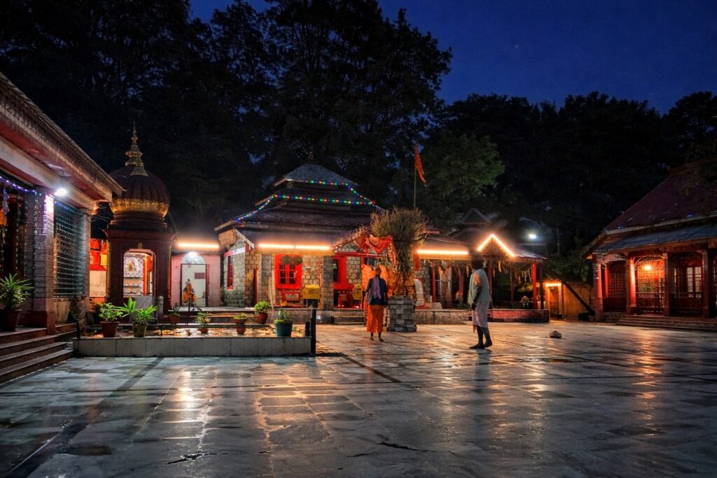 Aghanjar Mahadev Temple in Dharamshala at night with illuminated temple courtyard and reflections on wet stone floor