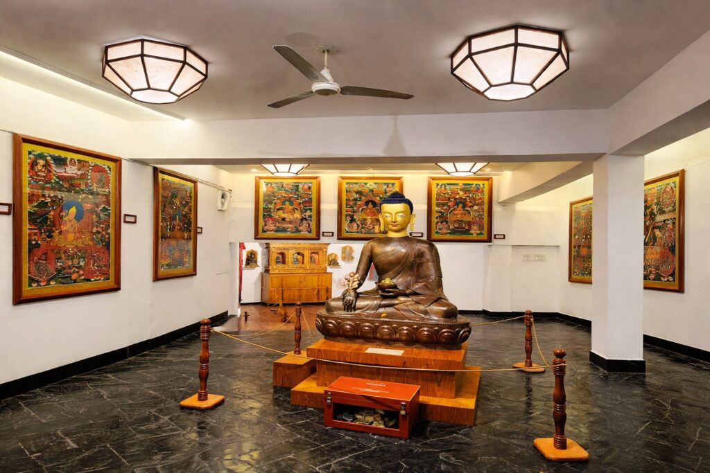 Buddha statue inside Norbulingka Institute Dharamshala surrounded by traditional Tibetan thangka paintings