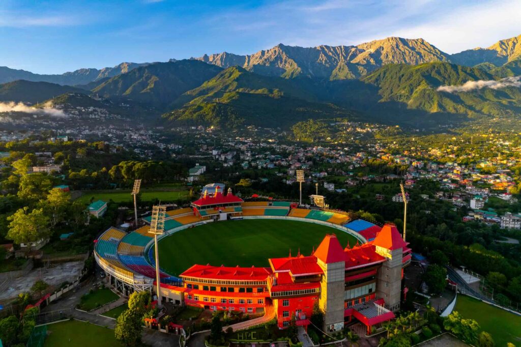 Aerial view of HPCA Stadium in Dharamshala with Dhauladhar mountains and town below, capturing the setting of Dharamshala IPL match 2026