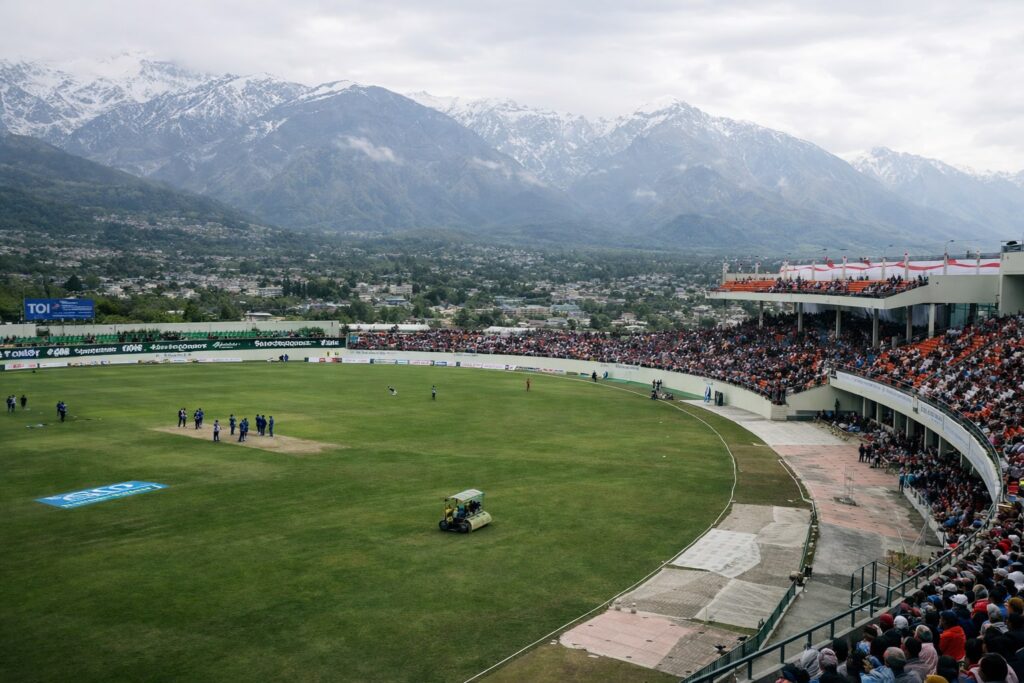 HPCA Stadium Dharamshala during a live cricket match with crowd and Dhauladhar mountains, representing Dharamshala IPL match 2026 schedule
