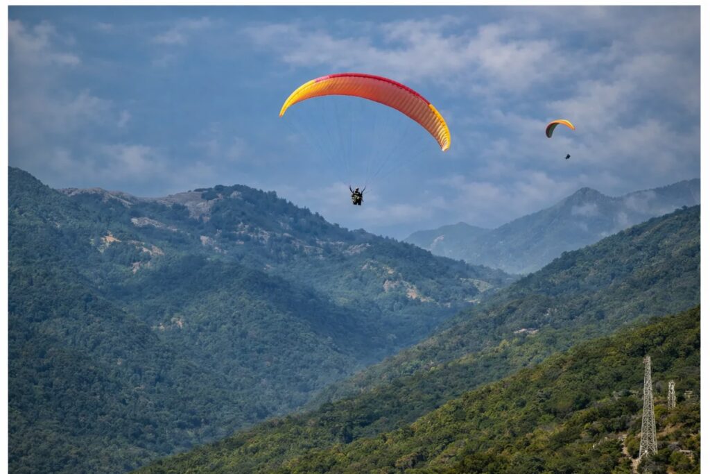 Solo female traveller paragliding over lush Himalayan mountains with scenic valley views