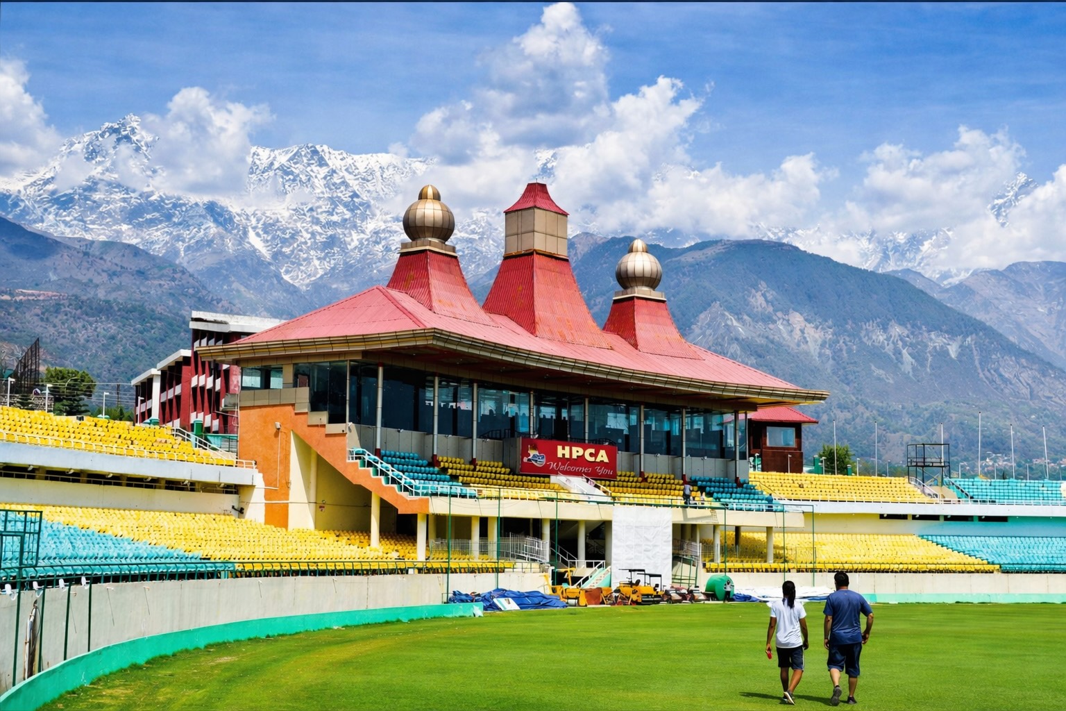 People walking on HPCA stadium ground with Dhauladhar mountains view near where to stay near HPCA stadium Dharamshala