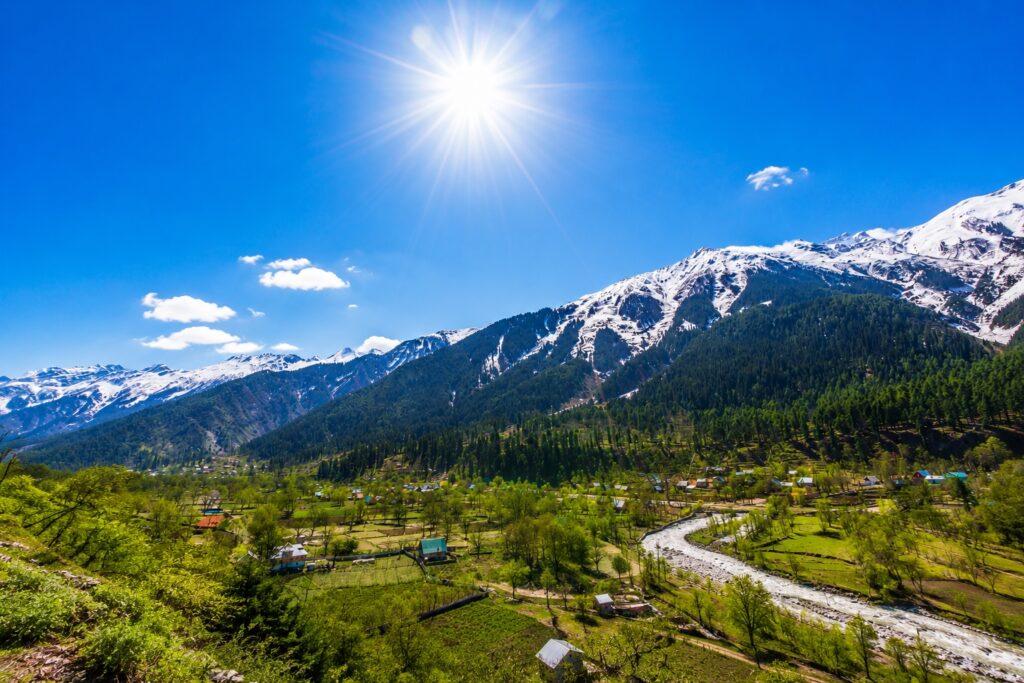 Dharamshala in June with clear blue skies, snow-capped Dhauladhar mountains, and bright sunshine