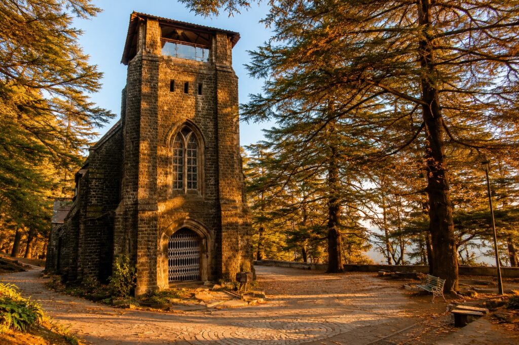 Best time to visit Dharamshala in autumn with golden cedar forests surrounding a historic stone church
