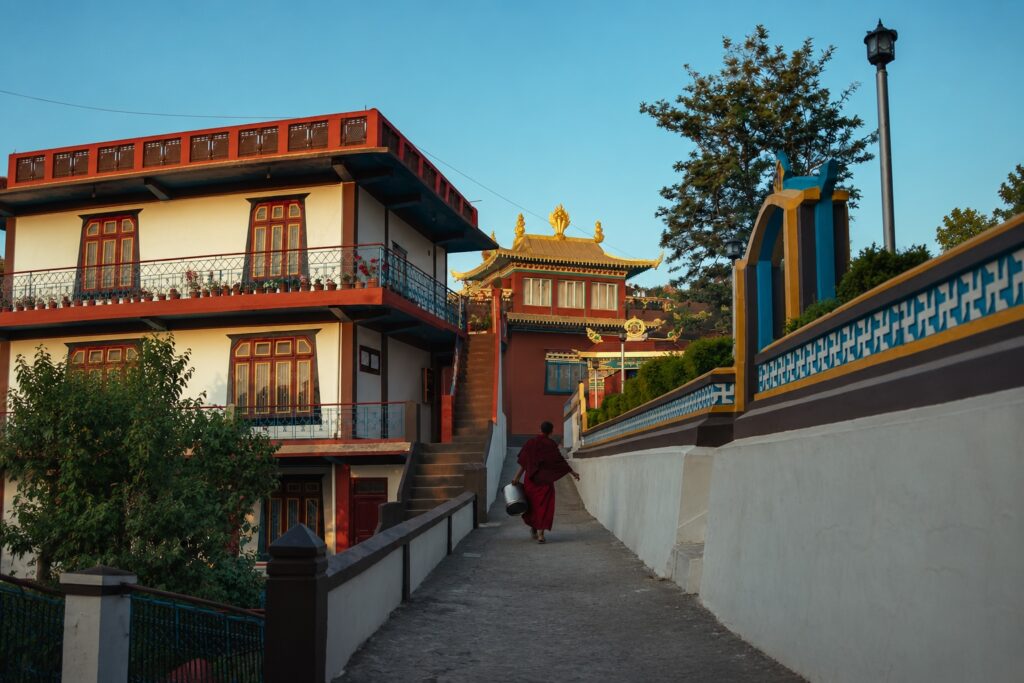 Monk walking along a pathway toward a traditional monastery in Bir Tibetan Colony, Himachal Pradesh.
