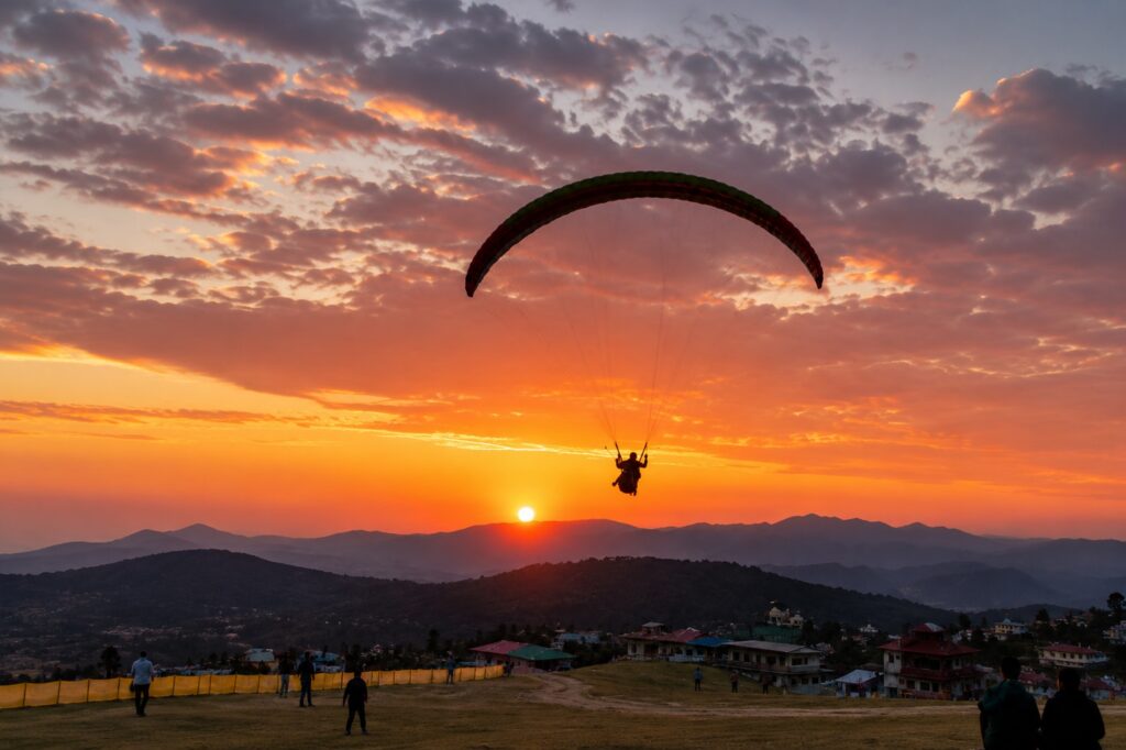 Paraglider flying over Bir Billing at sunset near a popular cafe in Bir