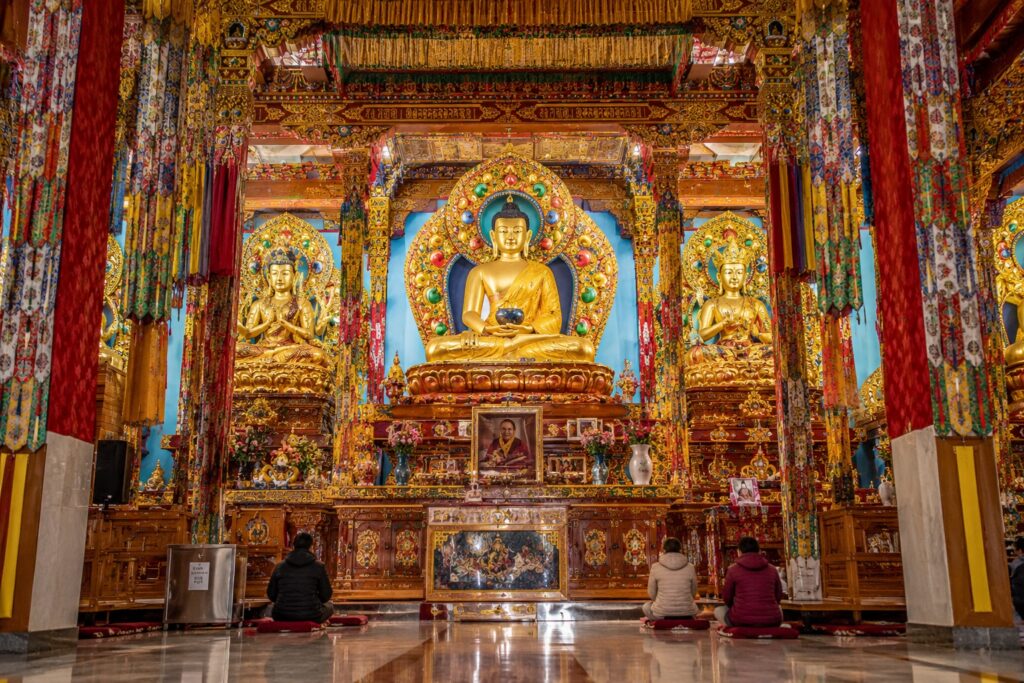 Dalai Lama Temple McLeodganj prayer hall interior with golden Buddha statues and Tibetan artwork