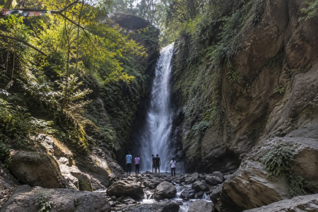 Visitors standing beneath a secluded forest waterfall near Bir, one of the most memorable things to do in Bir for nature lovers and adventure seekers.