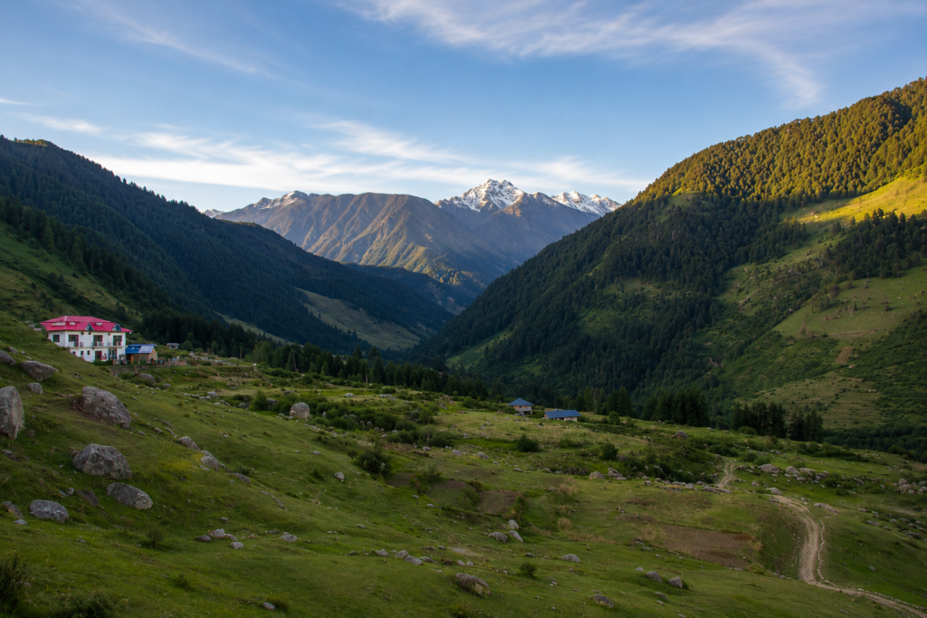 Scenic view of Rajgundha Valley with green meadows, pine-covered mountains, and distant Himalayan peaks, one of the most beautiful things to do in Bir.