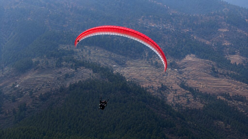 Solo Bir Billing paragliding flight soaring above the Himalayan valley with terraced hills and dense pine forests below.
