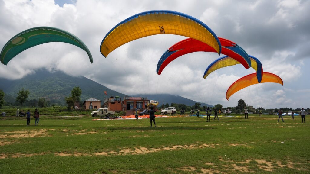 Colorful paragliders preparing for takeoff at the Bir Billing paragliding landing site with misty Himalayan mountains in the background.