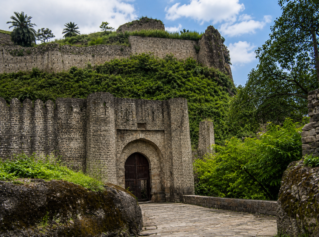 Ancient entrance of Kangra Fort in Kangra Valley surrounded by lush green hills and historic stone walls.